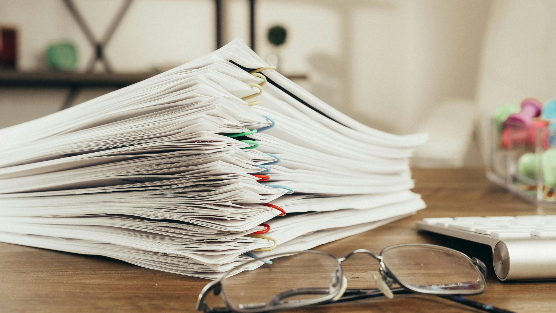 Nahaufnahme eines Stapels Büropapier auf einem Schreibtisch mit Brille, die die Ordnung unterstreicht.